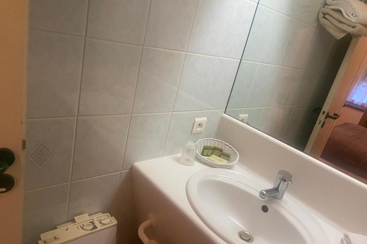 Un baño con un lavamanos blanco, un espejo y un perchero para toallas.