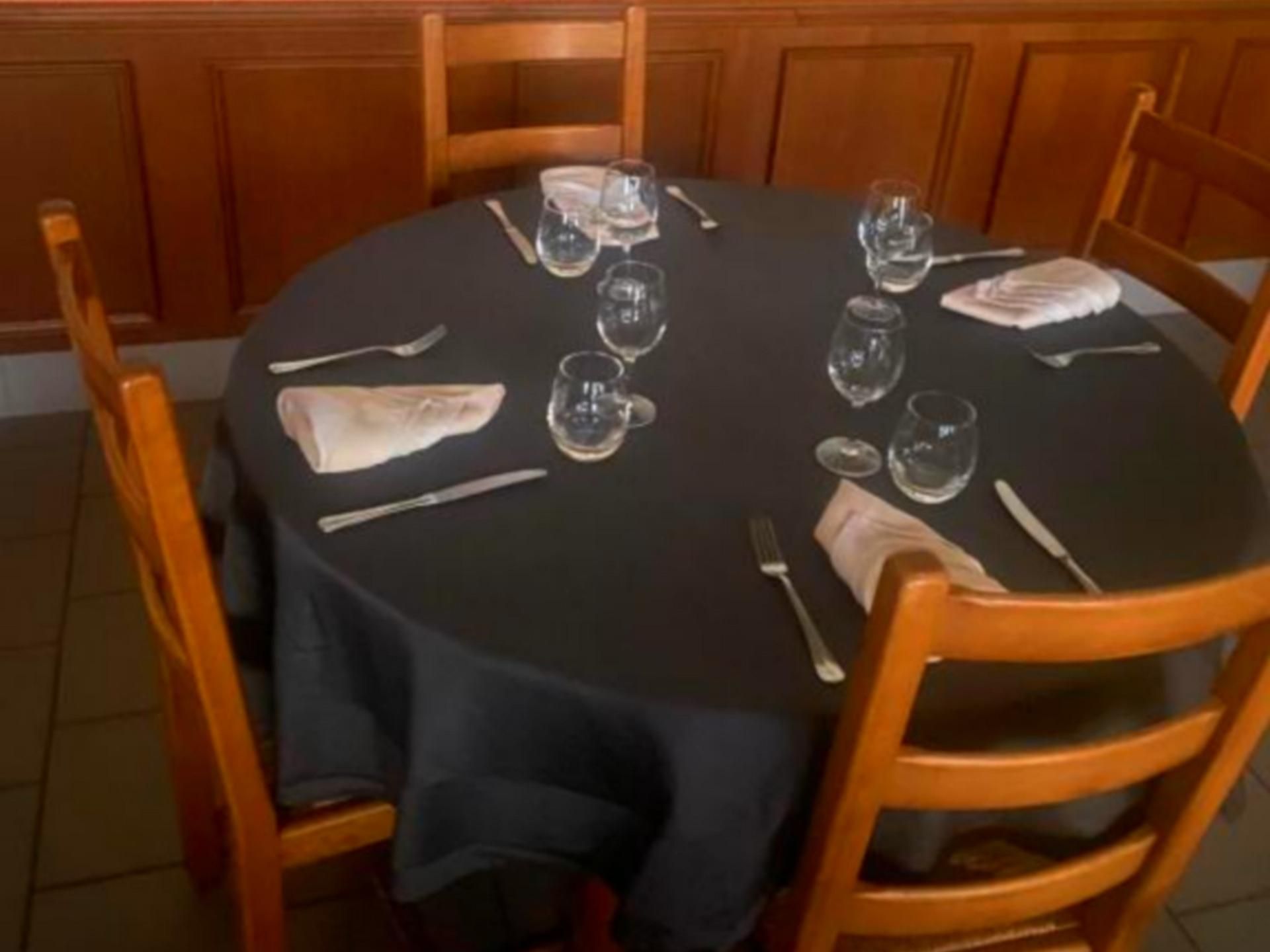 Une table de salle à manger ronde, recouverte d’une nappe noire, entourée de chaises en bois.