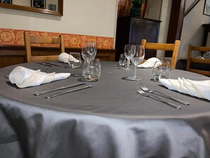 Mesa de comedor dispuesta con cubiertos y copas de vino, rodeada de sillas de madera.