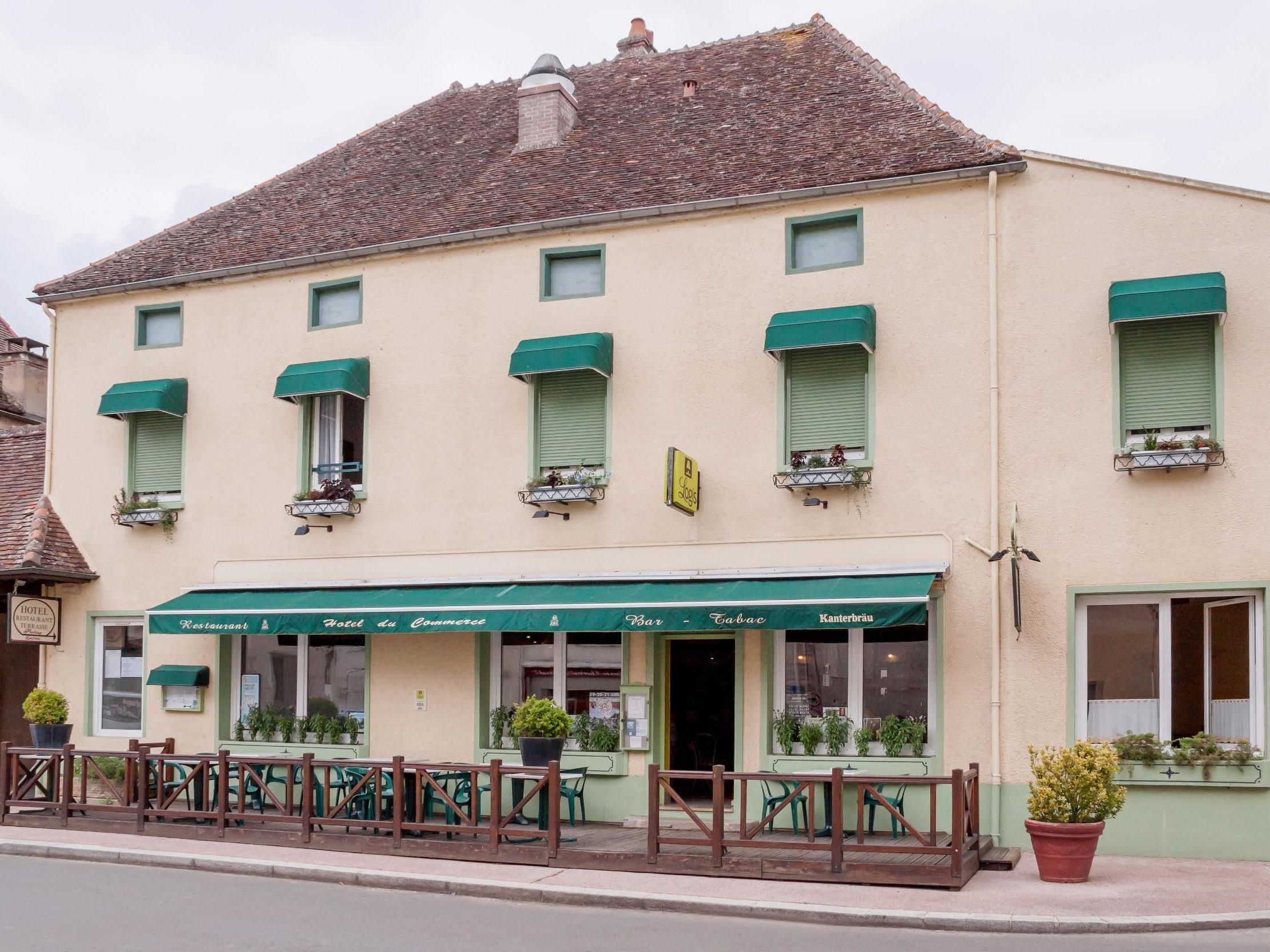 Ein Gebäude mit einer grünen Markise, auf der 'Restaurant Hotel du Commerce Bar - Tabac Kanterbräu' steht.