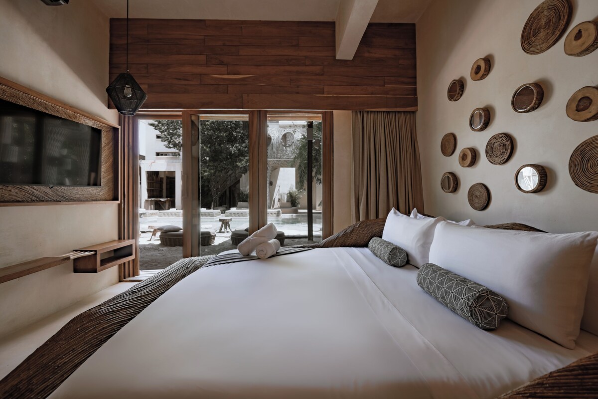 A large bed with white linens, a wooden headboard, and a view of the outdoors through large sliding doors.