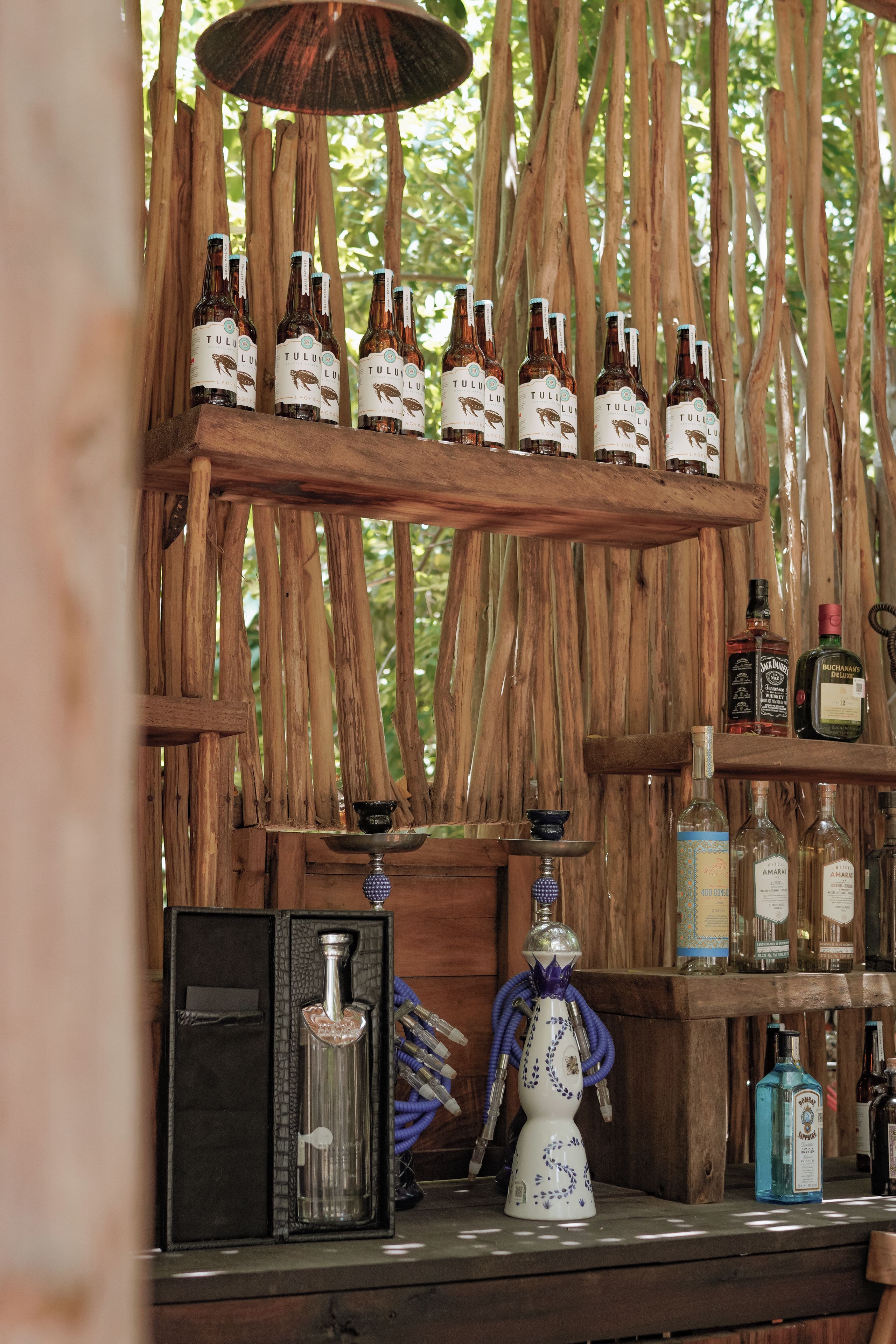 Una zona de bar con estantes de madera que exhiben botellas, un narguilé y varios líquidos en una barra.