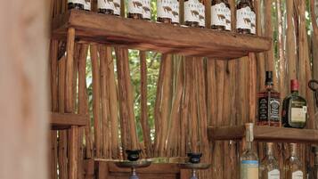 Una zona de bar con estantes de madera que exhiben botellas, un narguilé y varios líquidos en una barra.