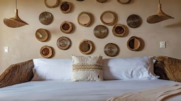 A bed with white linens and a patterned pillow, a wall with circular woven mirrors, and two hanging woven light fixtures.