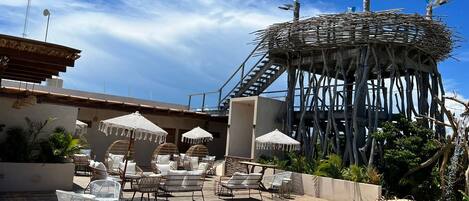 A pool area with lounge chairs, umbrellas, and a unique wooden structure.