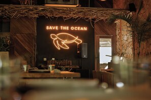 Un interior de restaurante con un letrero de neón que dice 'SAVE THE OCEAN' y una ilustración de una tortuga.