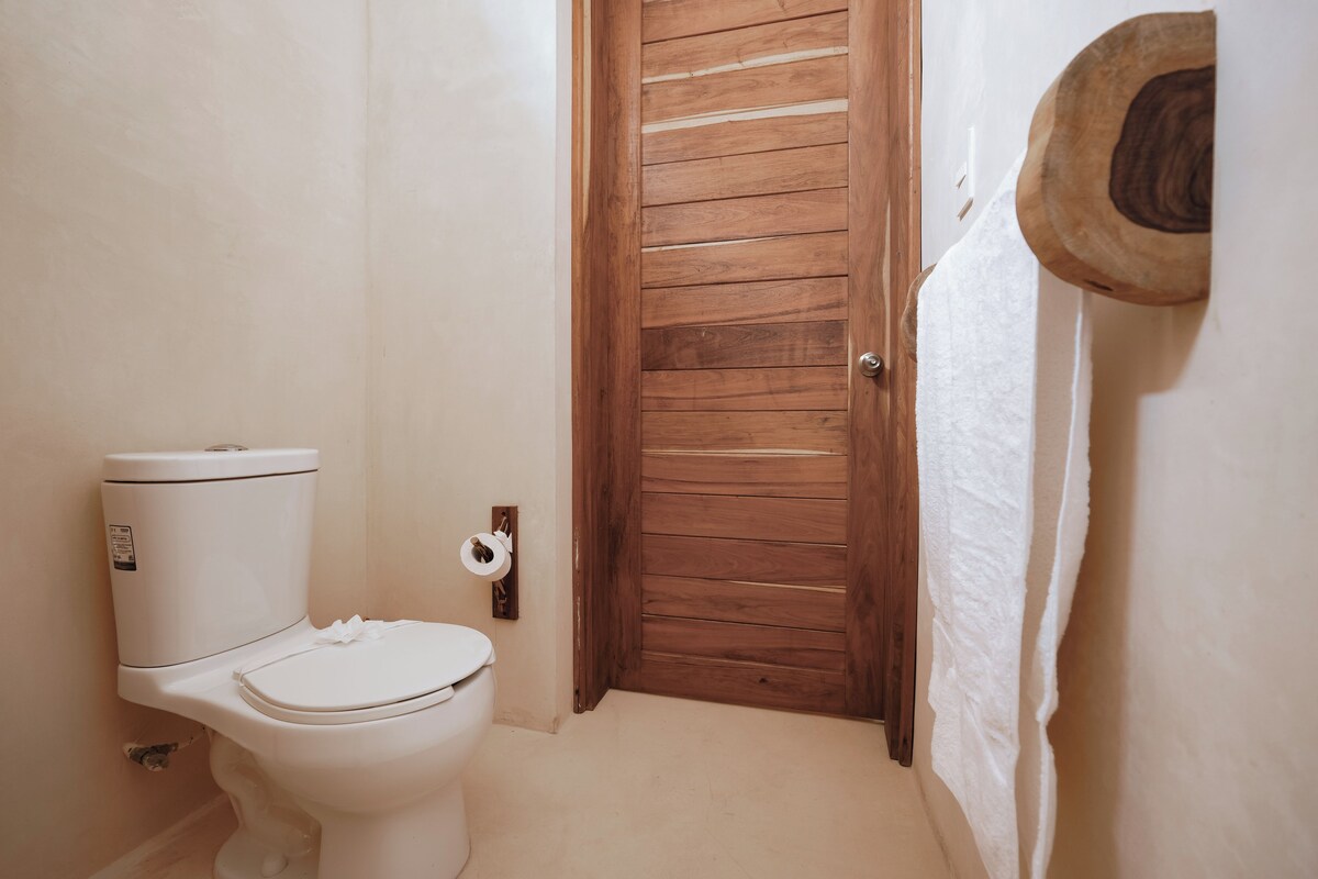 Un baño con inodoro, puerta de madera y un perchero para toallas.