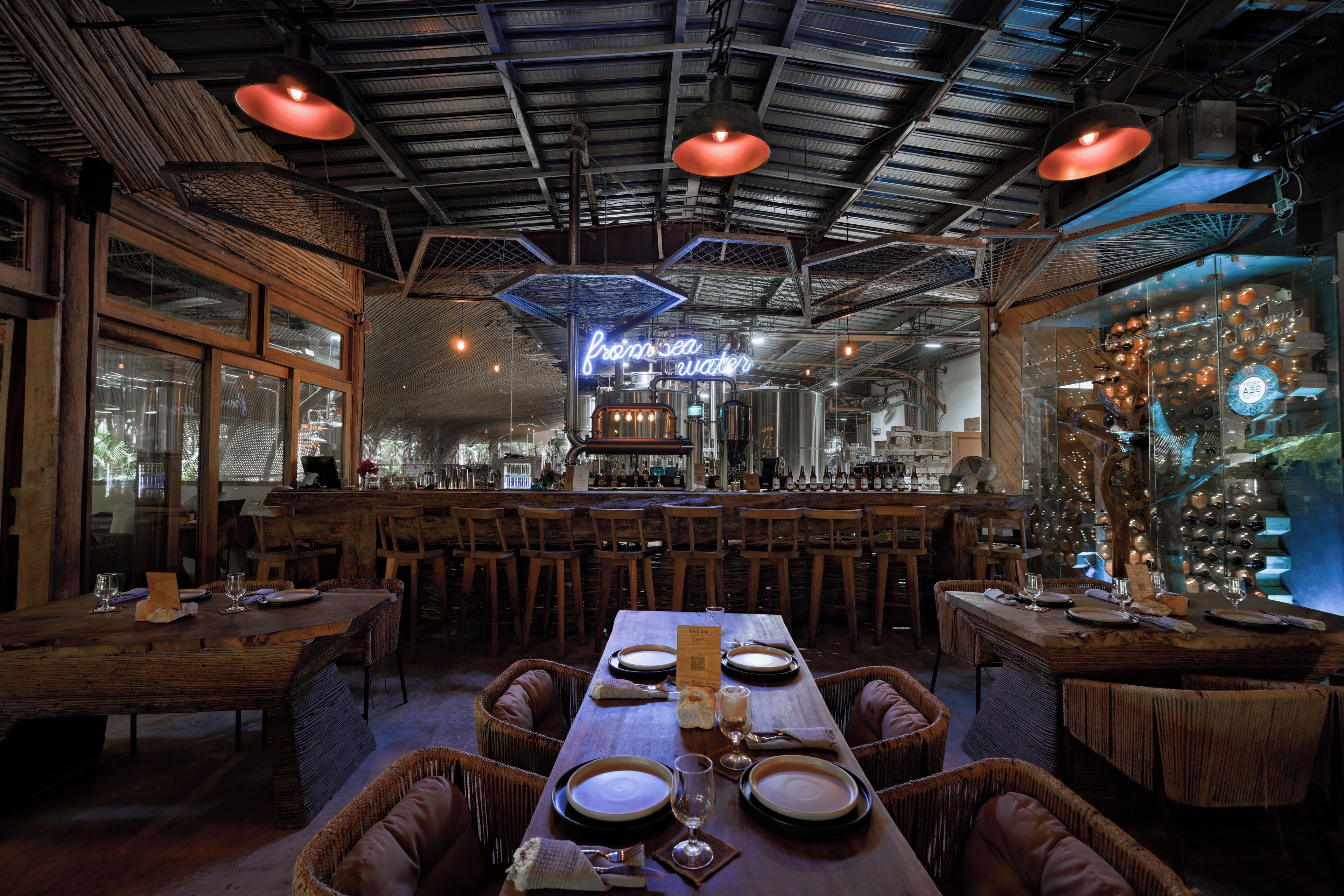 Un restaurante con mesas y sillas de madera, una zona de bar y un letrero de neón.