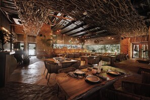 Restaurante com interior rústico, mesas de madeira e teto de materiais naturais.