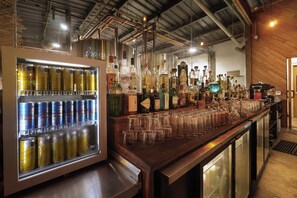 A bar area with a refrigerated drink dispenser, shelves of liquor bottles, and a bar counter with glasses. - Cervecería Tulum Boutique Hotel & Beer Spa (Tulum)
