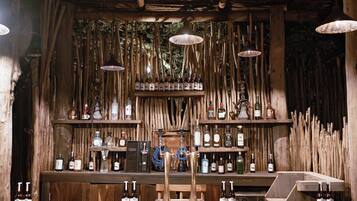 Un rústico área de bar con vigas de madera, luces colgantes y estantes llenos de botellas.