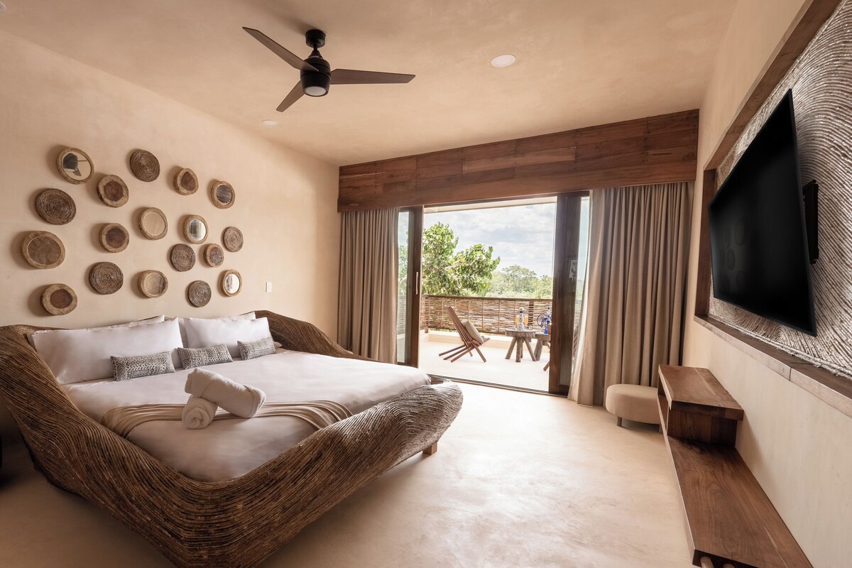 Un dormitorio amplio con una cama grande, un ventilador de techo y vistas al exterior a través de un ventanal corredero.