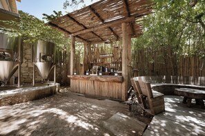 Zona de bar al aire libre con una pérgola de madera, columnas de piedra y una disposición de asientos.
