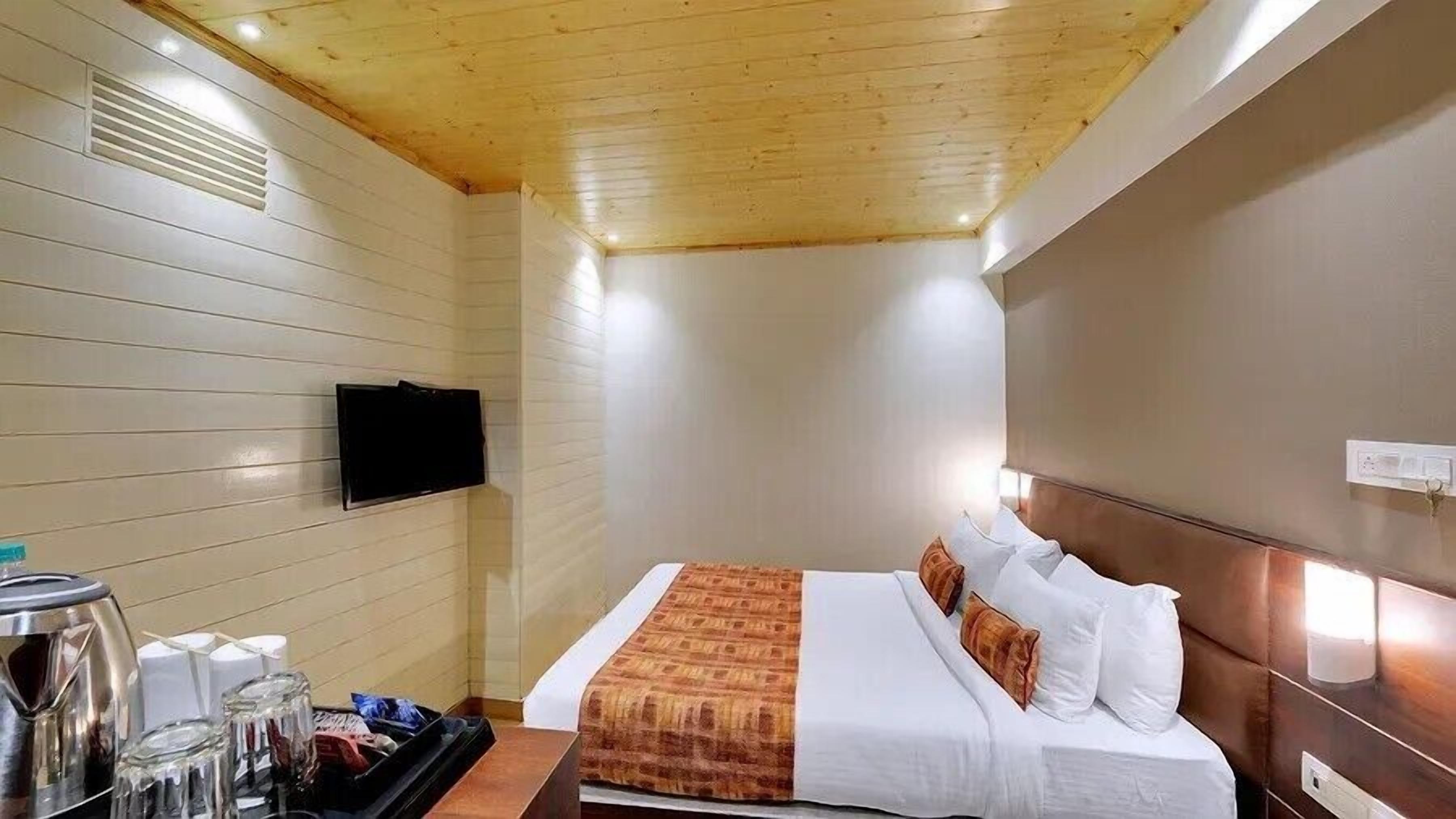 Ein Hotelzimmer mit Bett, Wandfernseher und kleinem Tisch mit Wasserkocher und Gläsern.