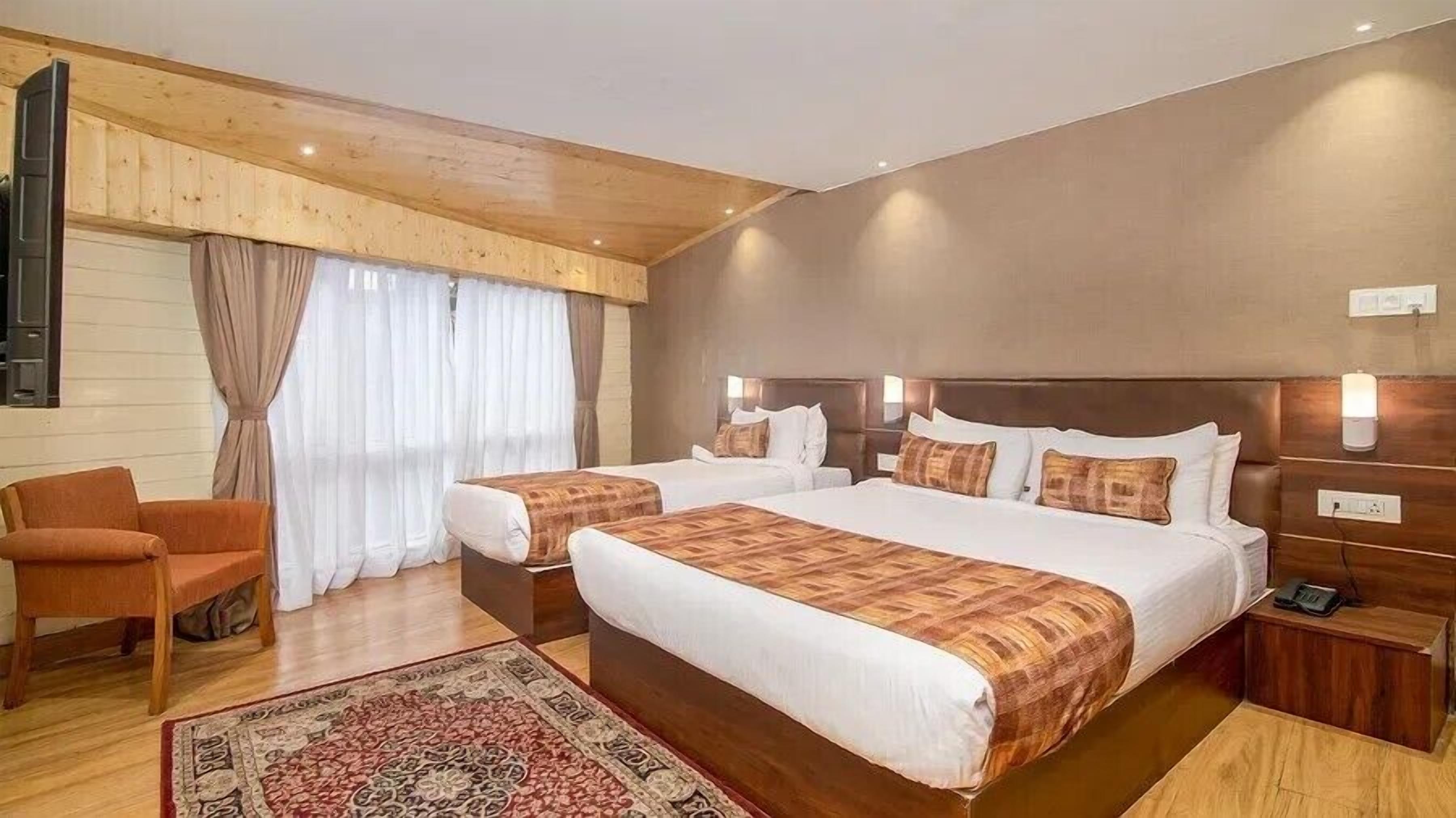 Ein Hotelzimmer mit zwei Betten, einer Holzbalkendecke, einem großen Fenster mit Vorhängen, einem Holzstuhl und einem Teppich.