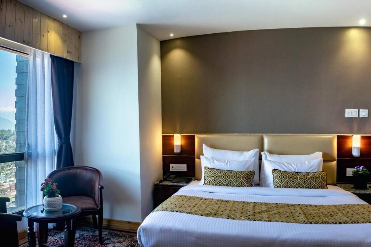 A hotel room with a large bed, a chair, a small table, and a view of a cityscape.