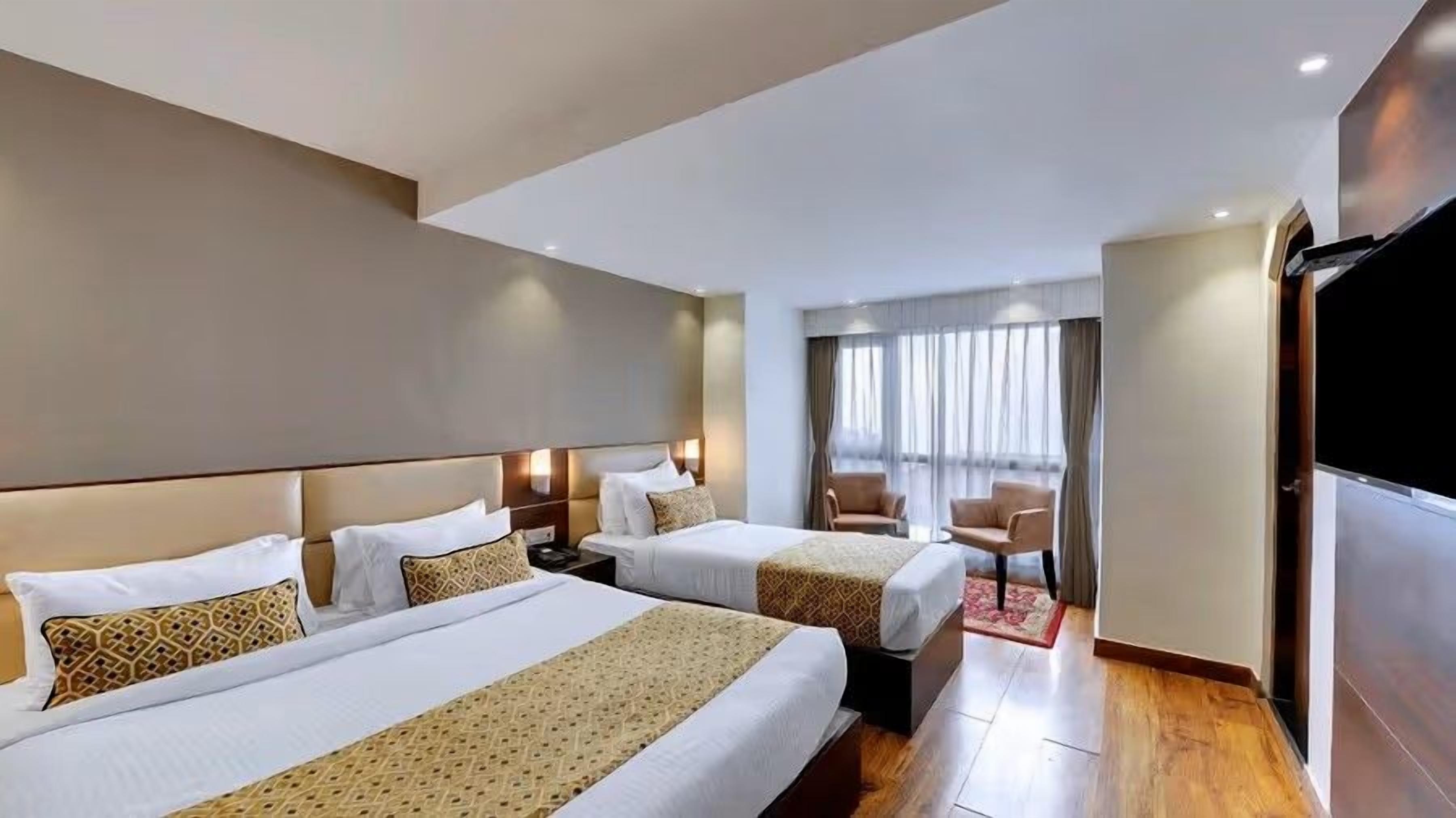 A hotel room with two beds, a TV, a desk, and a window with curtains.