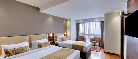 A hotel room with two beds, a TV, a desk, and a window with curtains.