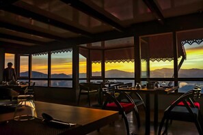 A restaurant with tables and chairs, large windows, and a view of the mountains. - Sumitel Vista 800m From Mall Road (Darjeeling)