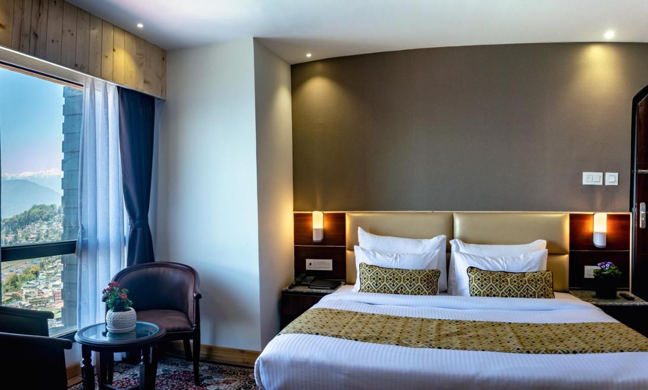 Habitación de hotel con una cama grande, una silla, una mesita y vistas a la ciudad.