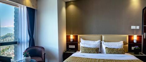 Habitación de hotel con una cama grande, una silla, una mesita y vistas a la ciudad.