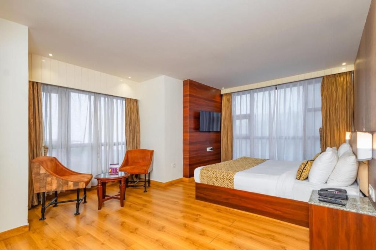 A hotel room with a wooden floor, a bed with white bedding, a desk with a chair, and a TV on the wall.