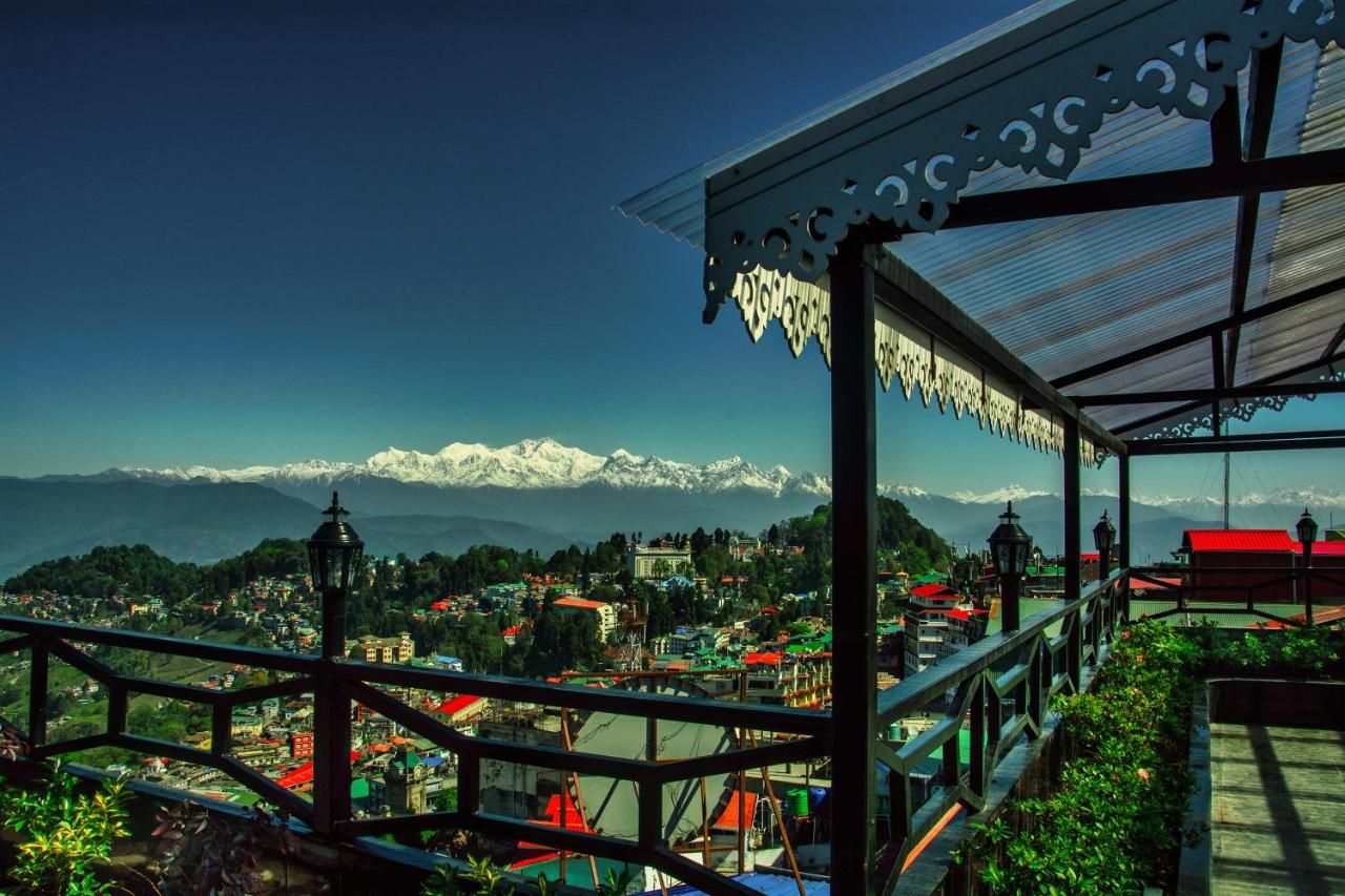 A scenic overlook with a metal railing, a view of a town below, and snow-capped mountains in the distance.