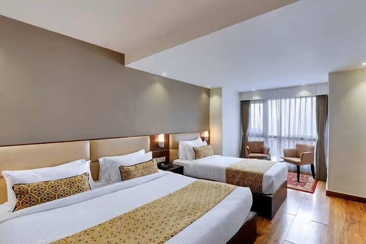 A hotel room with two beds, a TV, a desk, and a window with curtains.