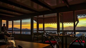 A restaurant with tables and chairs, large windows, and a view of the mountains. - Sumitel Vista 800m From Mall Road (Darjeeling)