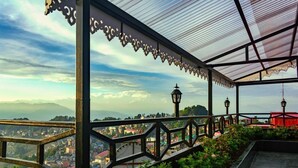 A covered outdoor area with a railing, a lamp post, and a view of a town and mountains in the background. - Sumitel Vista 800m From Mall Road (Darjeeling)