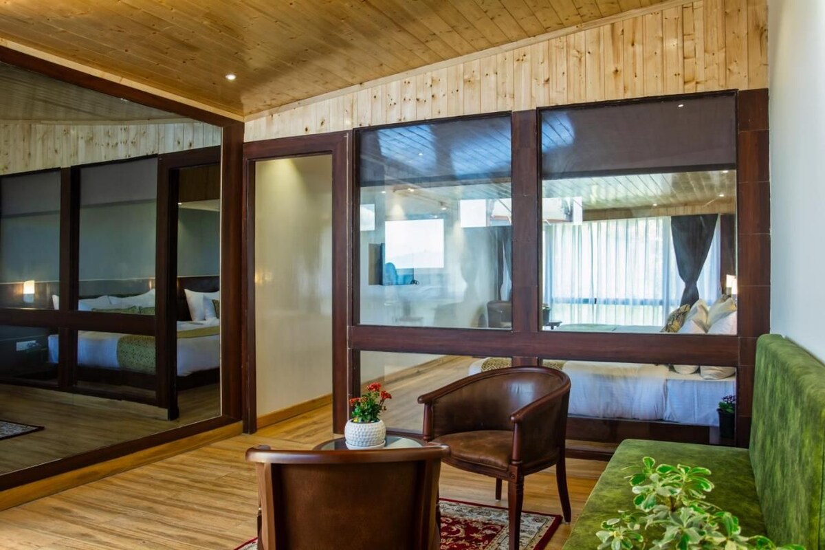 A room with a wooden ceiling, large windows, a bed, a green sofa, and a chair.