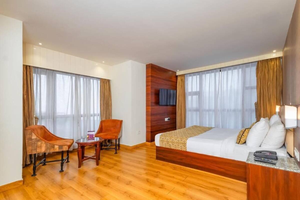 A hotel room with a wooden floor, a bed with white bedding, a desk with a chair, and a TV on the wall.