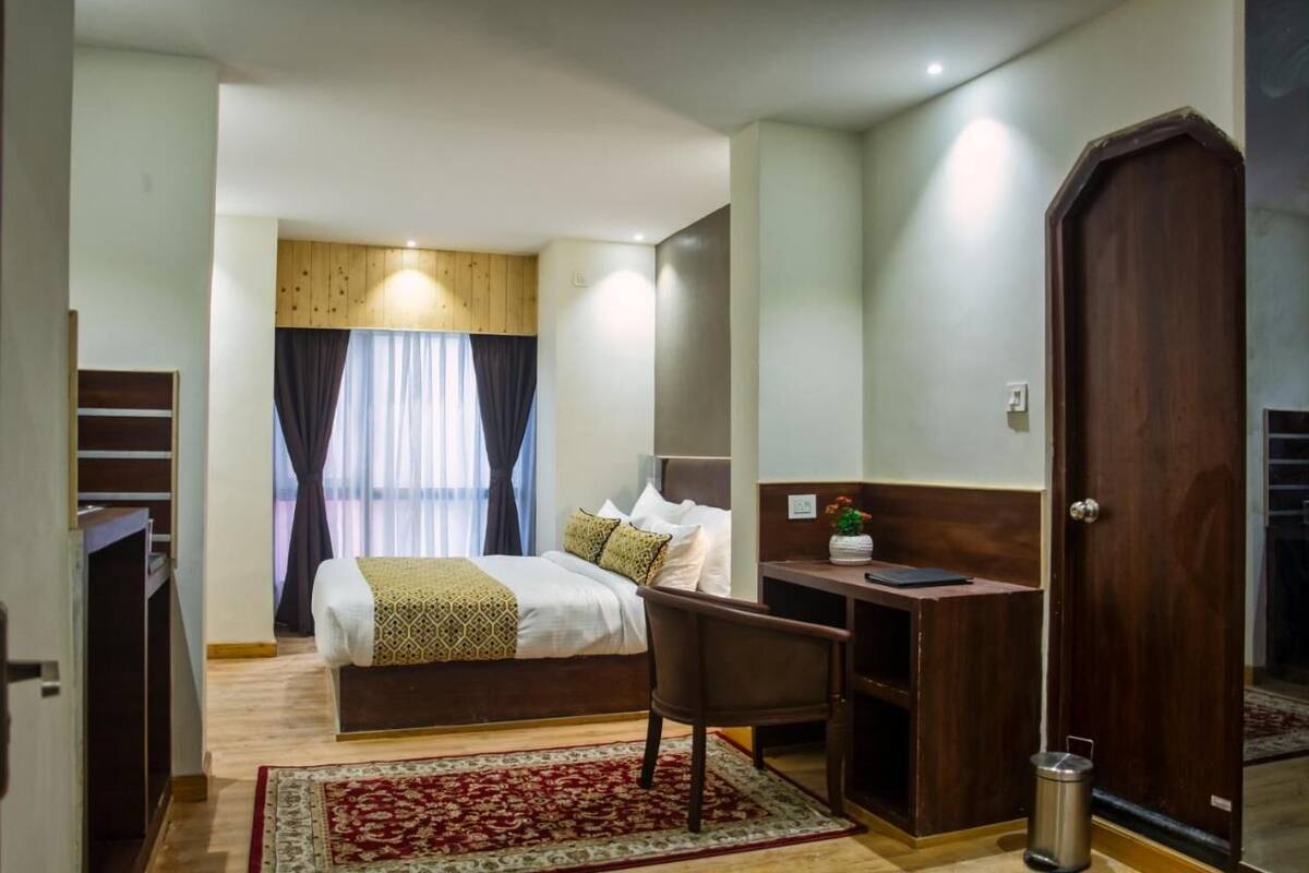 A hotel room with a bed, desk, chair, and a trash bin.