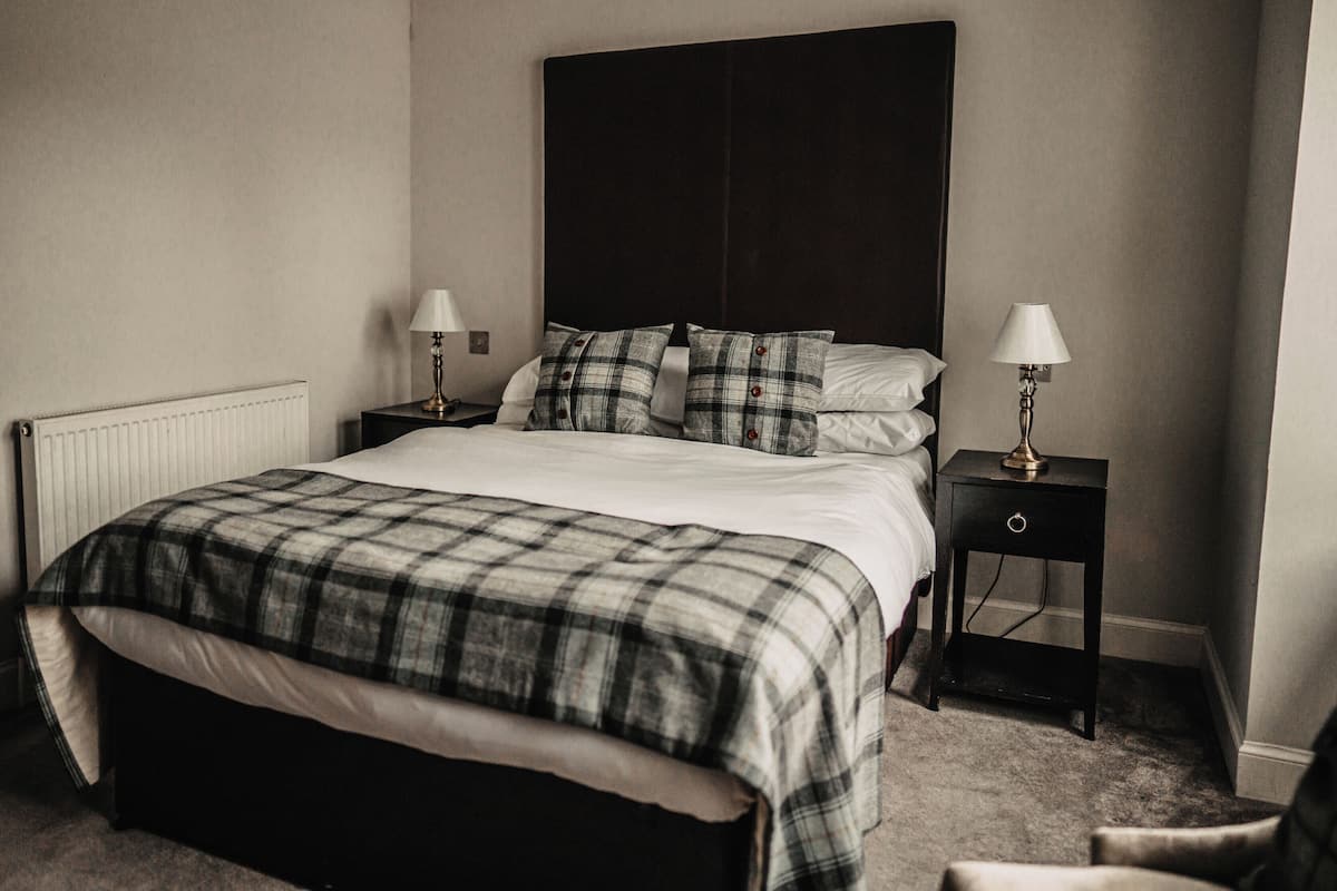 A neatly made bed with a plaid bedspread, two bedside tables with lamps, and a radiator on the wall.