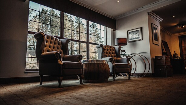 A room with large windows, two leather armchairs, a wooden coffee table, and a lamp.