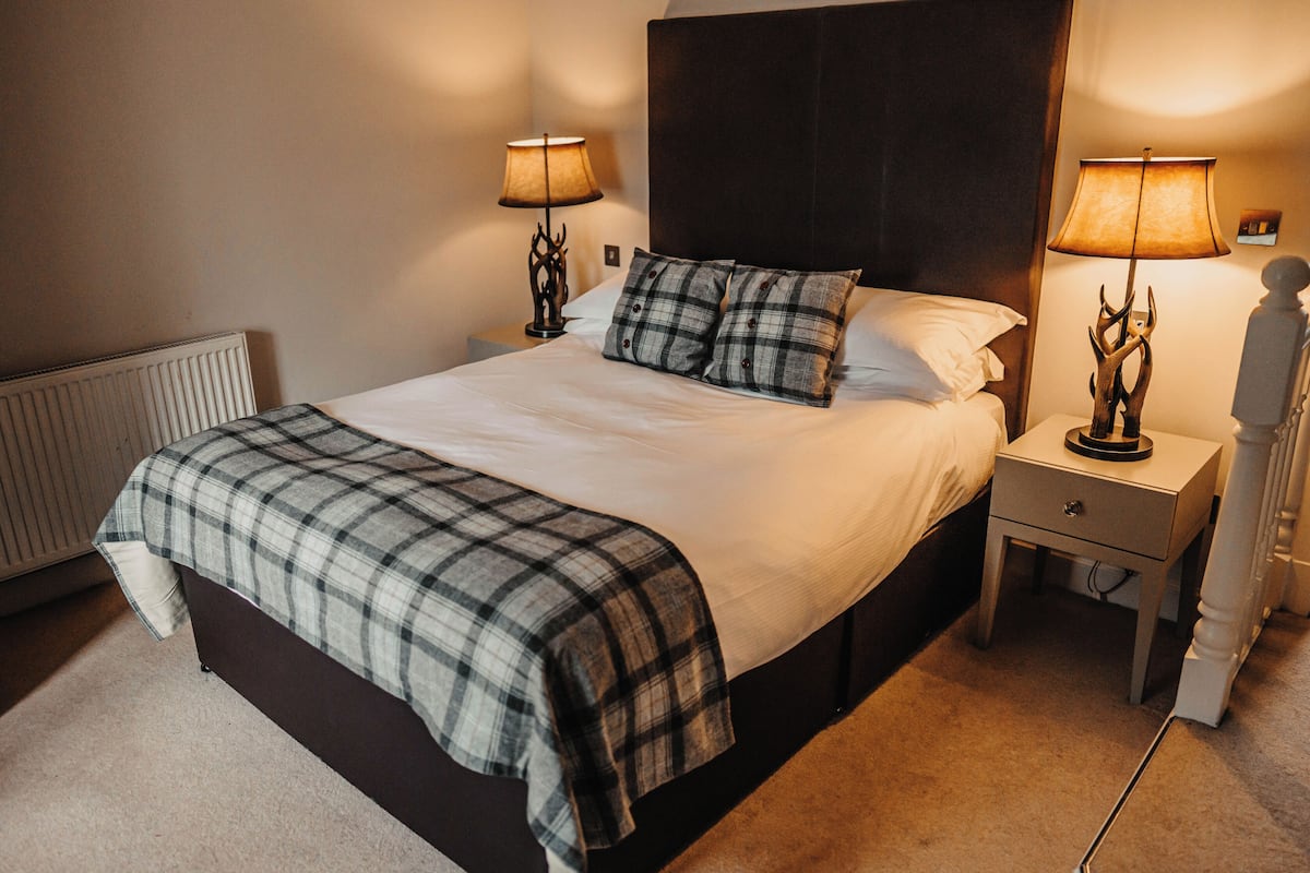 A neatly made bed with a plaid blanket, two bedside tables with lamps, and a radiator.