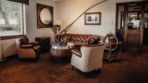 A room with a brown leather sofa, a round wooden coffee table, a lamp, a mirror, and a globe on a stand.