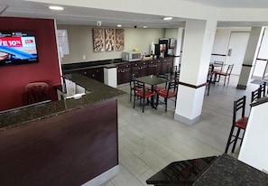 Eine Hotelhalle mit Rezeption, einem Essbereich mit Tischen und Stühlen sowie einer Küchenzeile mit Geräten.