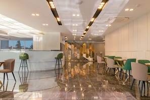 A modern interior with a reflective marble floor, green and beige chairs, and a central decorative wall. - Sabirlar City Suites Hotel (Trabzon)