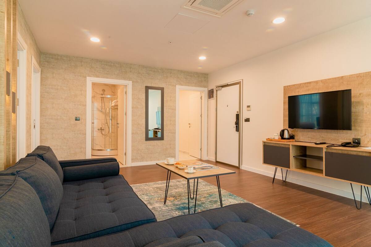 Ein modernes Wohnzimmer mit einem dunklen Sofa, einem Holztisch und einem an der Wand montierten Flachbildfernseher.