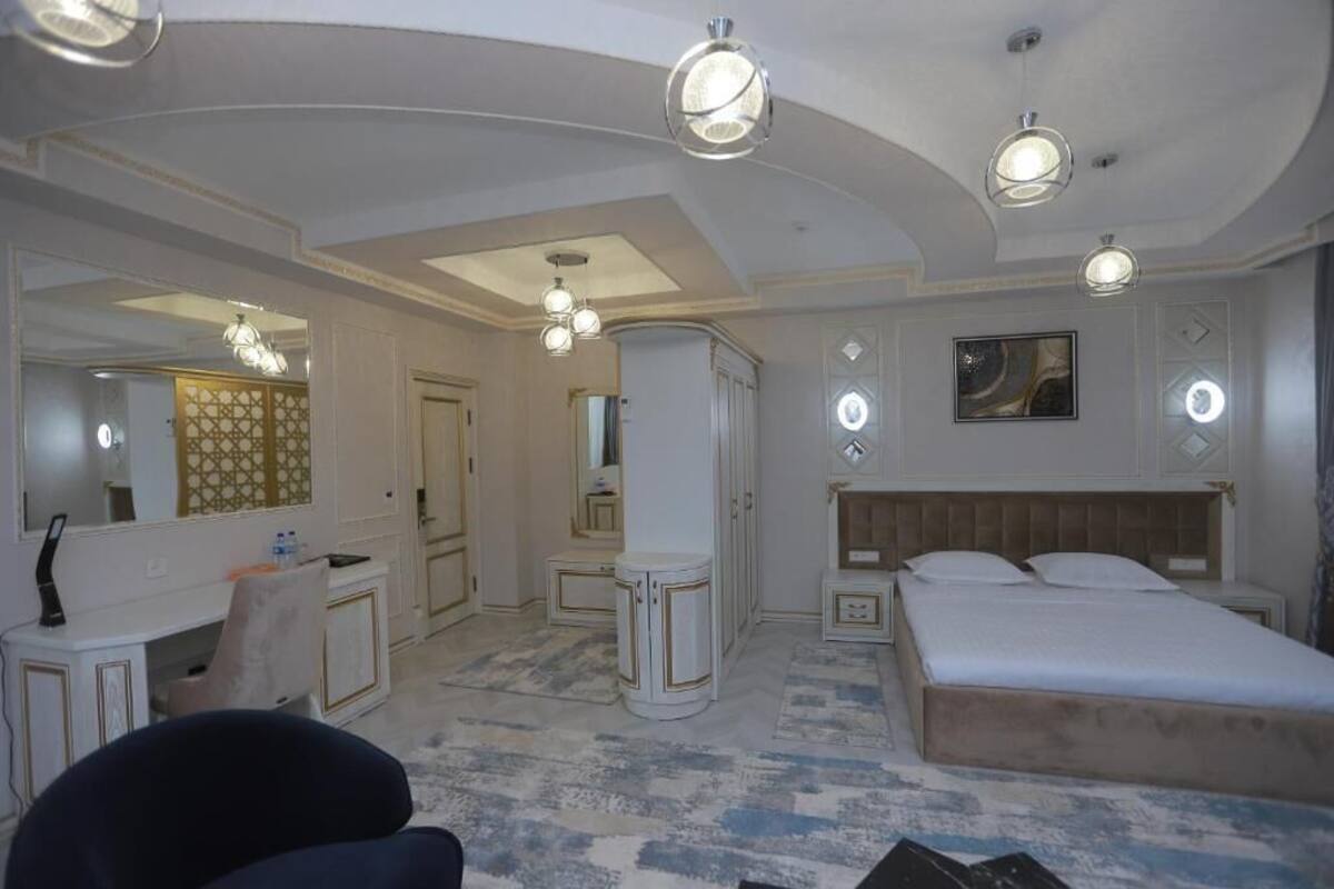 A hotel room with a large bed, a vanity with a mirror, a desk, and a chair. There are two pendant lights and a ceiling light.