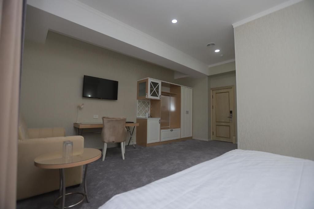 A hotel room with a bed, a small round table, a chair, a TV, a wardrobe, and a door.