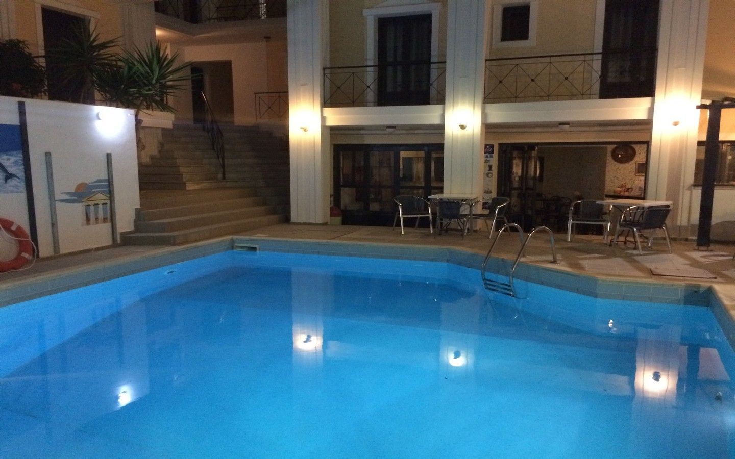 A swimming pool with steps leading up to a balcony, surrounded by outdoor furniture and a staircase.