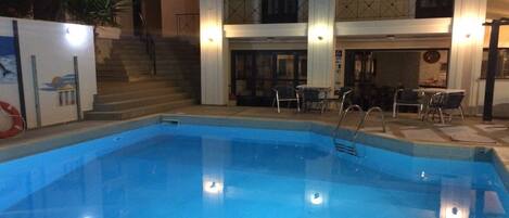A swimming pool with steps leading up to a balcony, surrounded by outdoor furniture and a staircase.