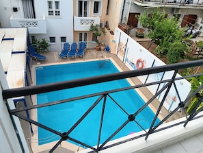 A swimming pool with a blue deck, surrounded by a white building with balconies.