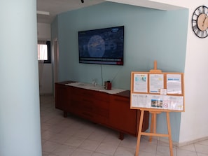 A reception area with a wooden desk, a bulletin board, a clock, and a television displaying a news channel.