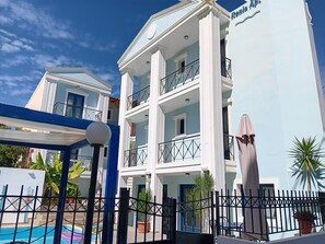 A multi-story hotel with balconies, a swimming pool, and a clear sky.