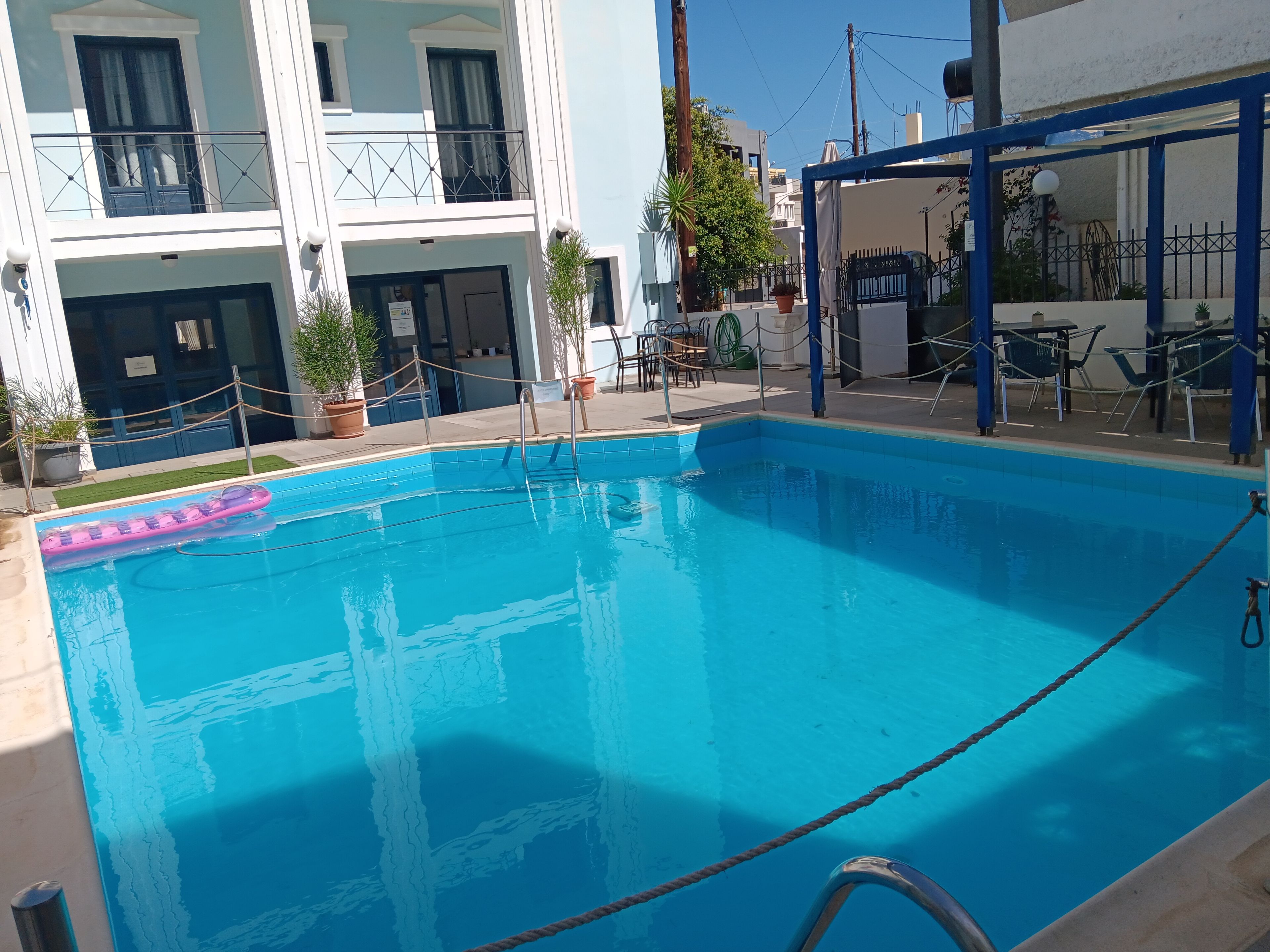 Una piscina con un flotador rosa, una zona de estar cubierta y un edificio con balcones.
