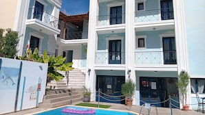 A multi-story hotel with balconies, a swimming pool, and a staircase leading to the entrance.