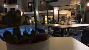 An indoor pool area with tables and chairs, a potted plant, and a dining area with a person seated.